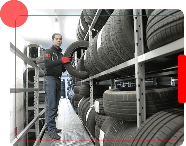 A man holding an tire in front of shelves filled with tires.